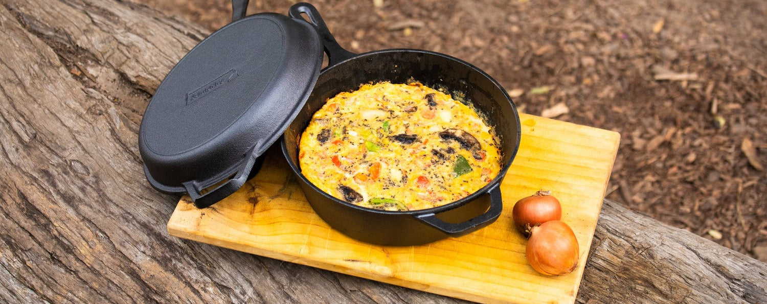 Cast Iron Combo Cooker 3.2 Quart holding a baked vegetable frittata outdoors on a wooden board, lid beside the pot.