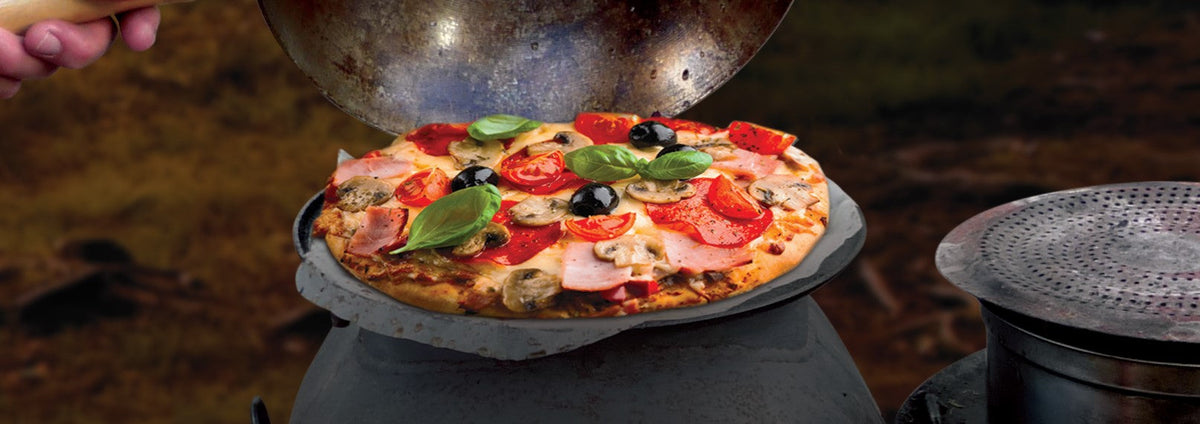 Homemade focaccia pizza cooking on an Ozpig outdoor cooker with fresh basil, olives, tomatoes and mushrooms.