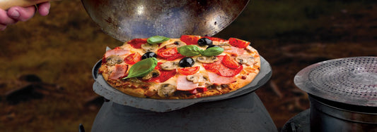 Homemade focaccia pizza cooking on an Ozpig outdoor cooker with fresh basil, olives, tomatoes and mushrooms.