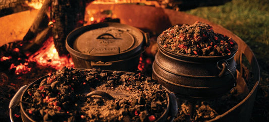 Cast iron pots and camp ovens covered in hot coals cooking over a fire pit at night.