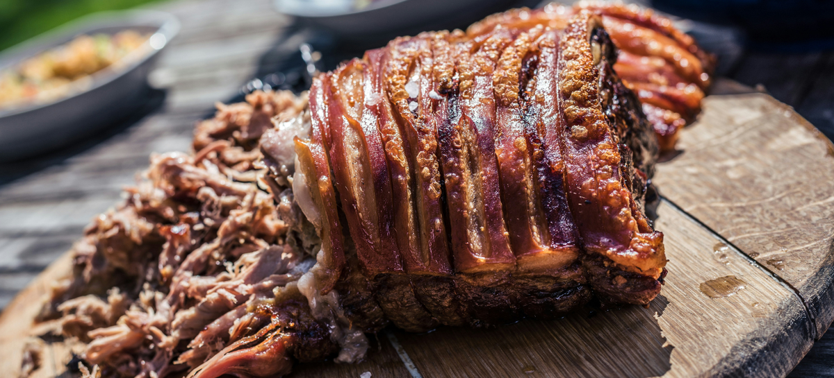 Tender smoked pulled pork with crackling prepared in a smoker and served on a rustic wooden board.