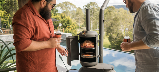 Two men checking food cooking inside an Ozpig Oven Smoker while standing by a pool with drinks.