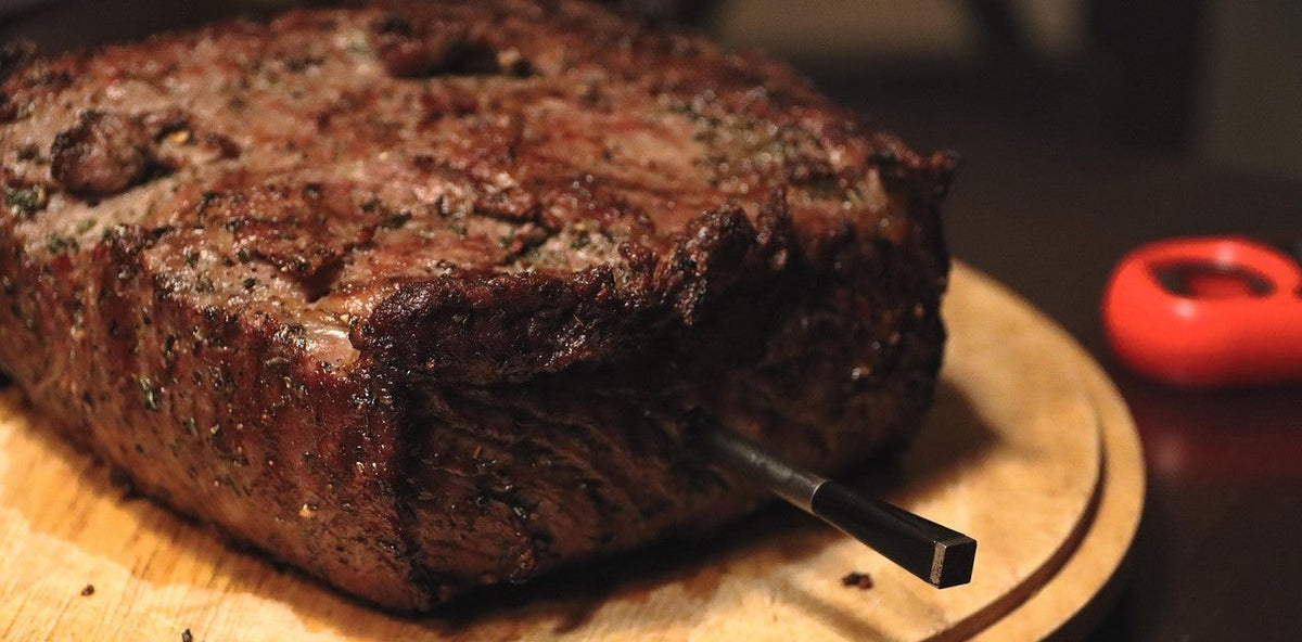Slow-cooked beef spit roast seasoned with a dry rub on a wooden carving board.