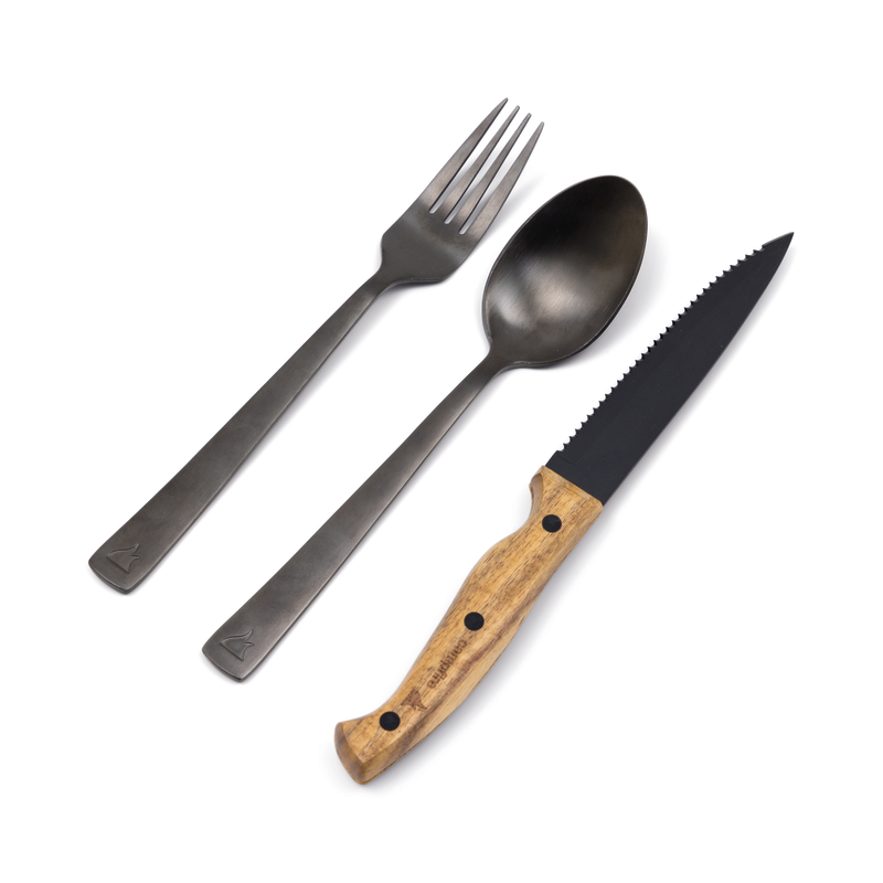 A fork and spoon with a matte black finish from the Campfire 12pc Cutlery Set are arranged next to a serrated knife with an acacia wood handle, all displayed on a white background.