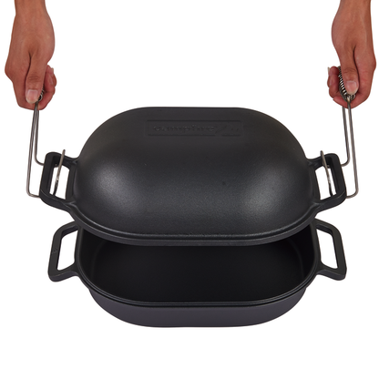 A person holds the handles of a Campfire Combo Camp Oven, with its black cast iron lid raised above the base to reveal both parts—ideal for campfire cooking and ready to use with its pre-seasoned finish.