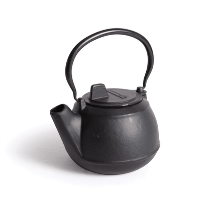 A 2 Quart Cast Iron Kettle by Campfire, featuring a small, black design with a curved handle and short spout, is placed on a white surface.