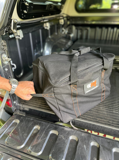 A person places an Ozpig Series 2 Heavy Duty Storage Bag—crafted from durable canvas with strong handles and internal pockets—onto the bed of a pickup truck. The prominent "Ozpig" logo is clearly visible on the side of the zippered bag.