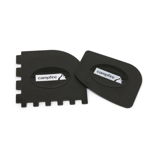 The Campfire Scraper Set 2PK includes two oval-shaped black plastic pan scrapers, each featuring the “Campfire” label. Designed for camp cooking and cleaning cast iron cookware, one scraper has a smooth edge while the other offers both smooth and notched edges. Both scrapers are shown on a white background.