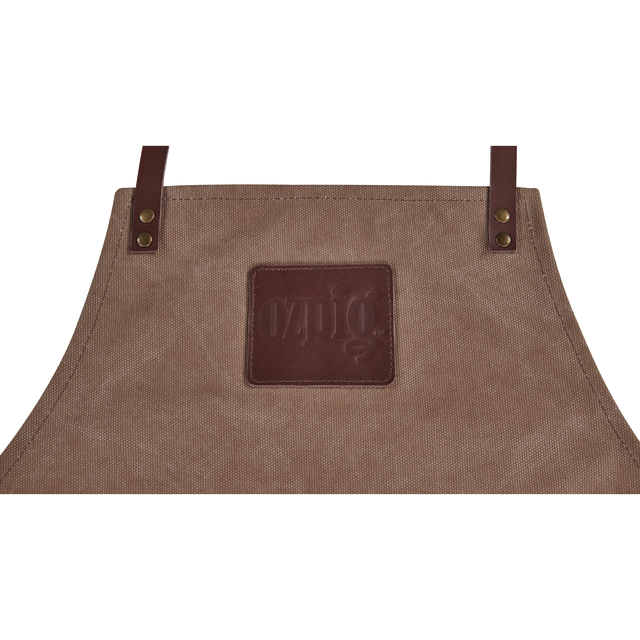 The Ozpig Apron by Ozpig features leather detailing, durable canvas straps, brass rivets, and a rectangular embossed leather patch stitched on the front center. The top part of this apron is visible in the image.