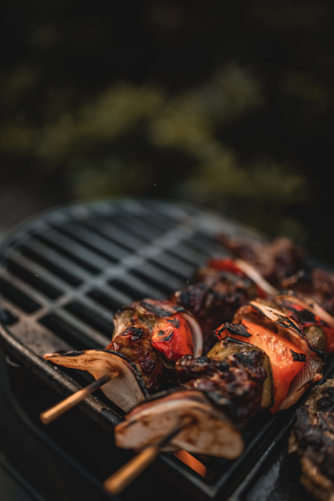 Grilled vegetable and meat skewers with onions and peppers sizzle on the Ozpig Big Pig Chargrill by Ozpig, infusing every bite with an irresistible wood-fired taste, set against a blurred green background.