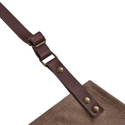 Close-up of the Ozpig Apron by Ozpig, showing its brown leather strap with metal rivets and buckle, leather detailing, and attachment to a durable canvas apron.