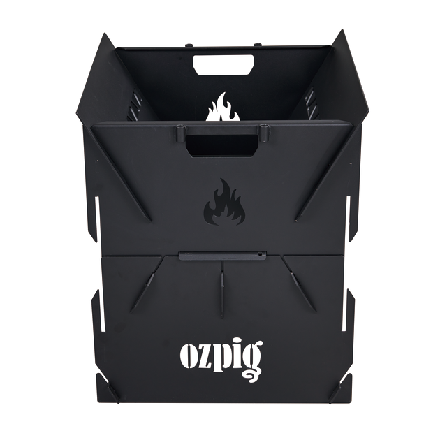 The Ozpig 3-in-1 Flat Pack Fire Pit is a black, square metal camping fire pit with angled sides, top handles for easy transport, the Ozpig name in white on the front, and a flame cutout above it.