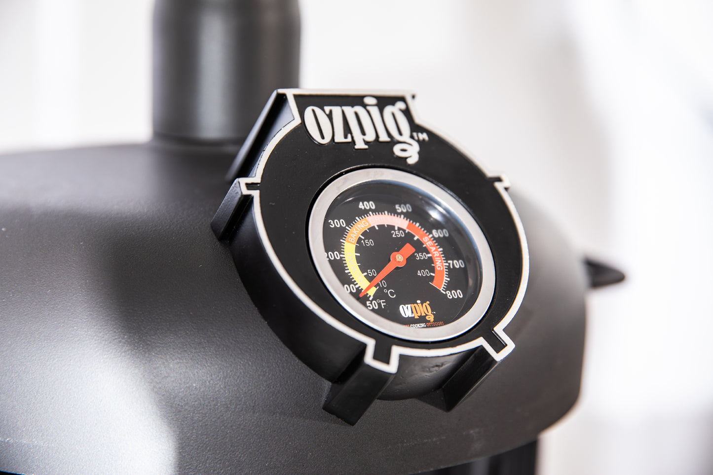 Close-up of an Ozpig thermometer gauge mounted on the black metal surface of the Ozpig Oven Smoker by Ozpig, displaying a temperature reading around 250°F (120°C) with bold white and red markings—ideal for creating that authentic woodfired flavour during your outdoor cooking sessions.